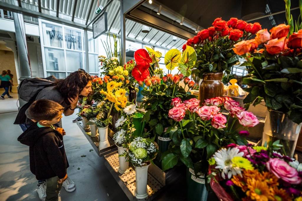 Mãe e filho observam flores coloridas numa banca de mercado