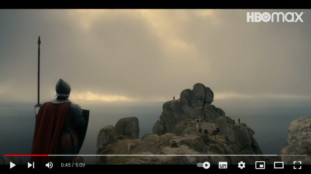 Reprodução de um trecho da série A Casa do Dragão que mostra o elenco no topo de uma montanha com gigantescas formações rochosas