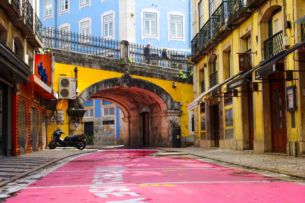 Casario amarelo e azul e rua pintada de cor de rosa no bairro Cais do Sodré, em Lisboa