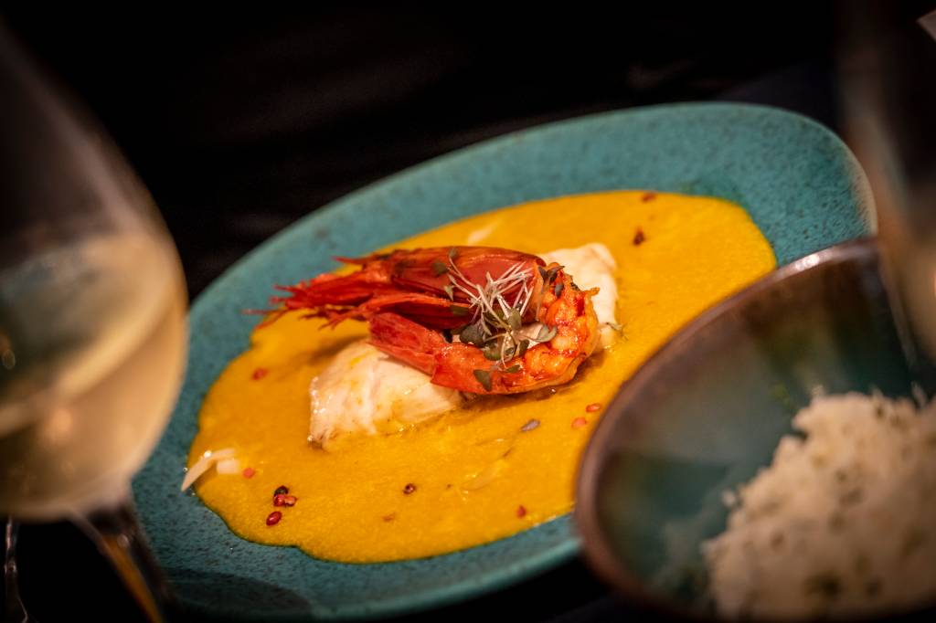 Prato do restaurante com um creme amarelo na base, um filé de peixe e um grande camarão ao centro