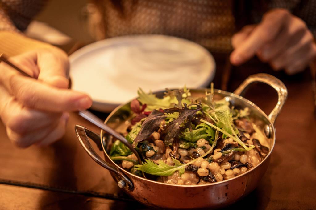 Prato do restaurante Bartolomeu servido numa panelinha de cobre: grãos de cevadinha com cogumelos e folhas verdes