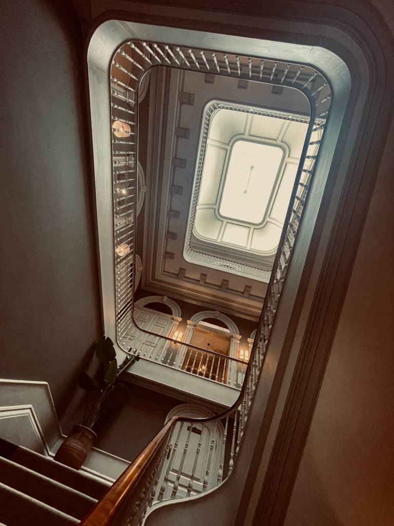 Foto de baixo para cima mostrando a escadaria do hotel Torel 1884, com uma clarabóia no topo