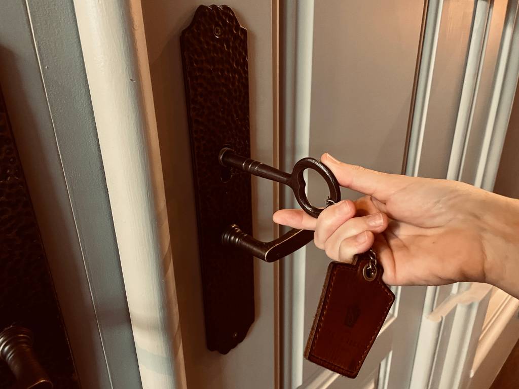 Uma grande chave na fechadura da porta, com uma mão girando para abrir