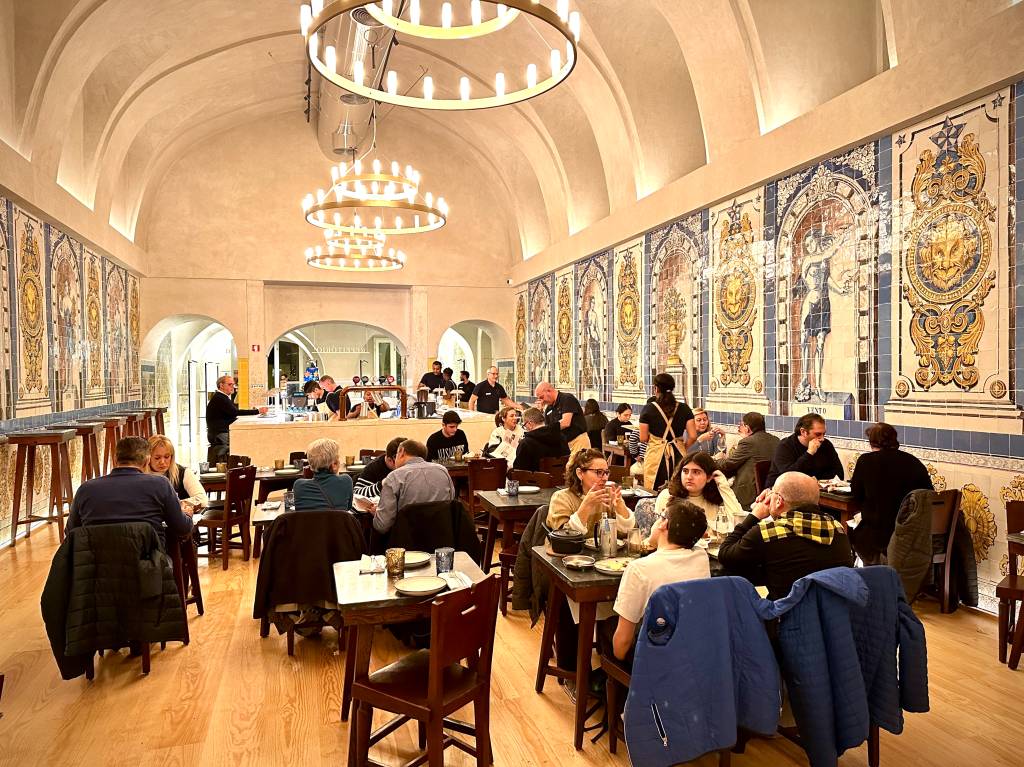 Um dos ambientes da cervejaria dedicado aos petiscos, com mesas mais informais e painéis de azulejo coloridos nas paredes
