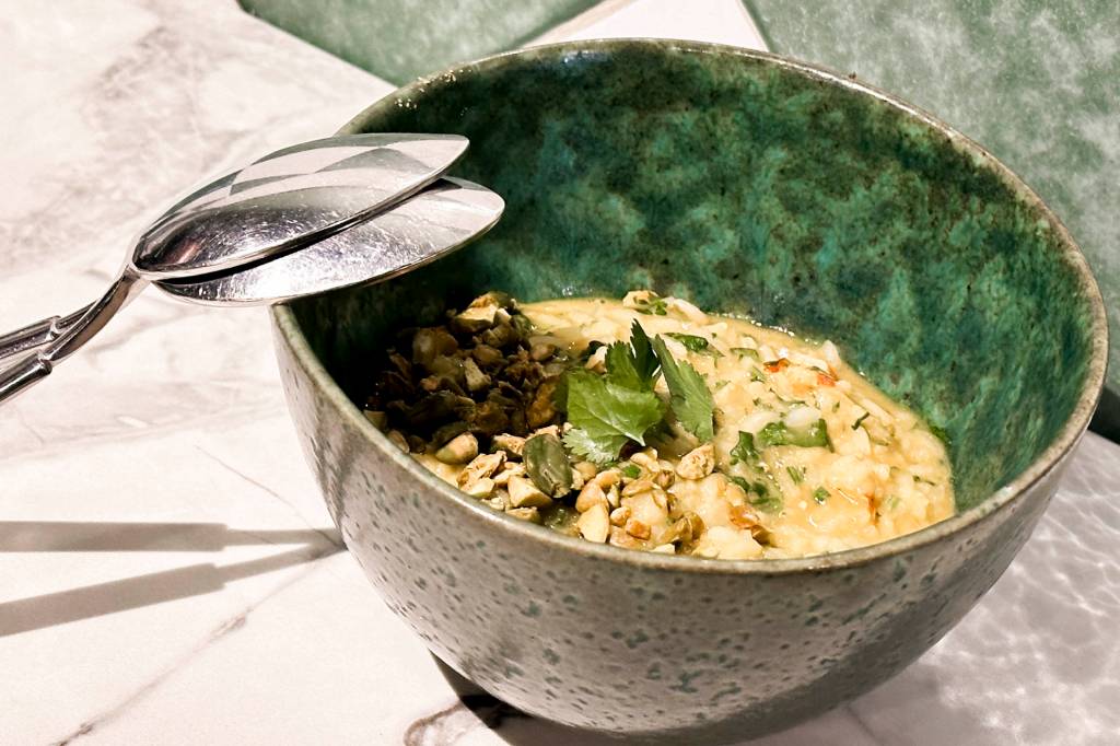Prato cremoso com grãos de cevada e enguia servido num bowl verde, coroado por folhinhas e pistaches