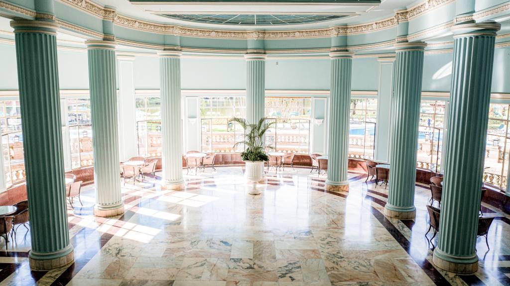 A fotografia colorida mostra um salão azul com muitas janelas e colunas com aspecto clássico