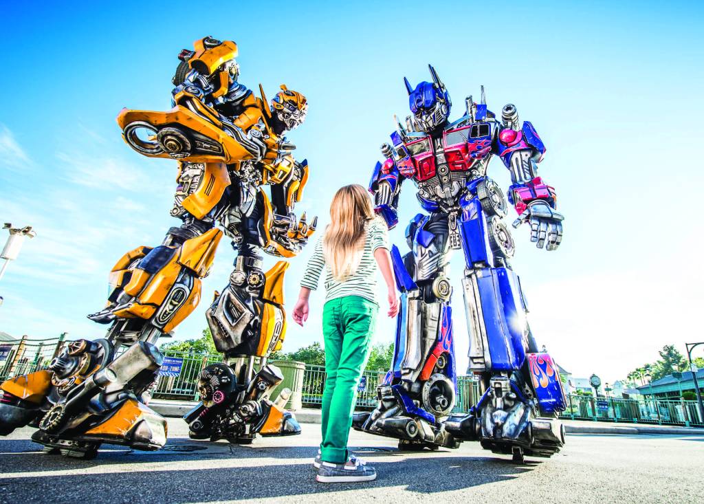 A imagem mostra uma criança em frente a dois robôs gigantes