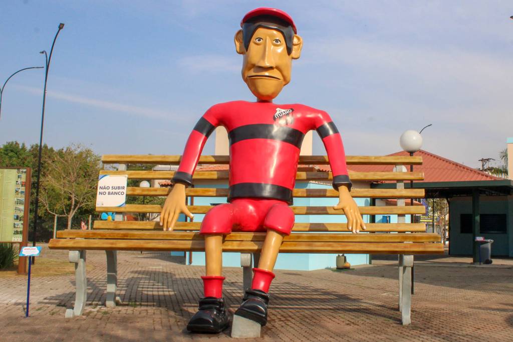 A foto mostra uma escultura gigante de um homem vestindo uma camisseta vermelha e preta do time ituano
