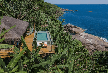 A imagem mostra uma cabana com piscina no meio de uma plantação de bananas, em frente ao mar