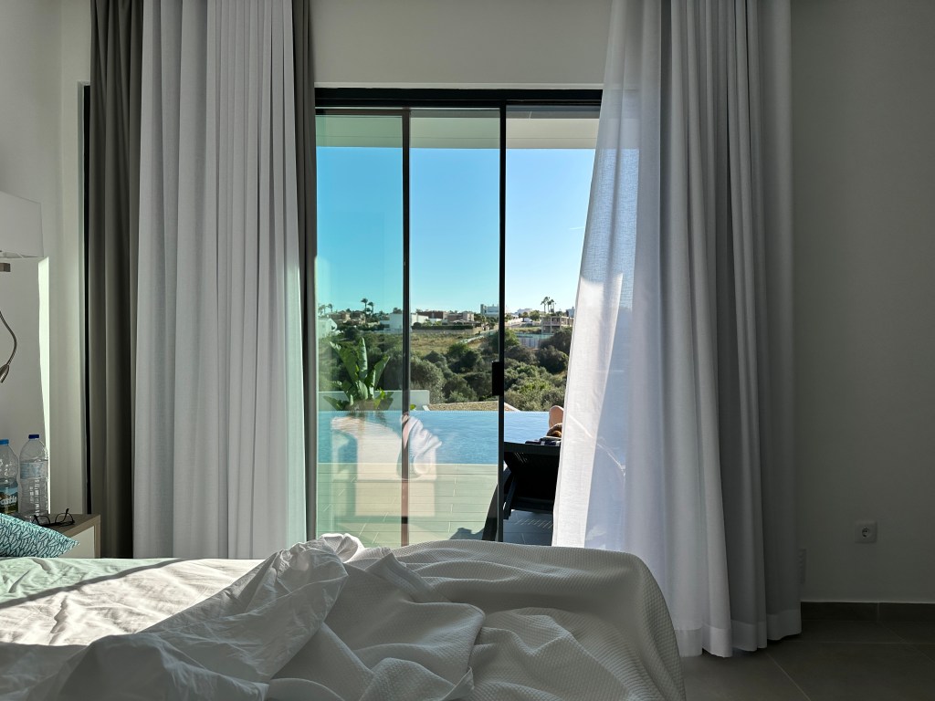 IMG_9334 Quarto da pousada com a cama em primeiro plano e uma porta de vidro que se abre para a piscina