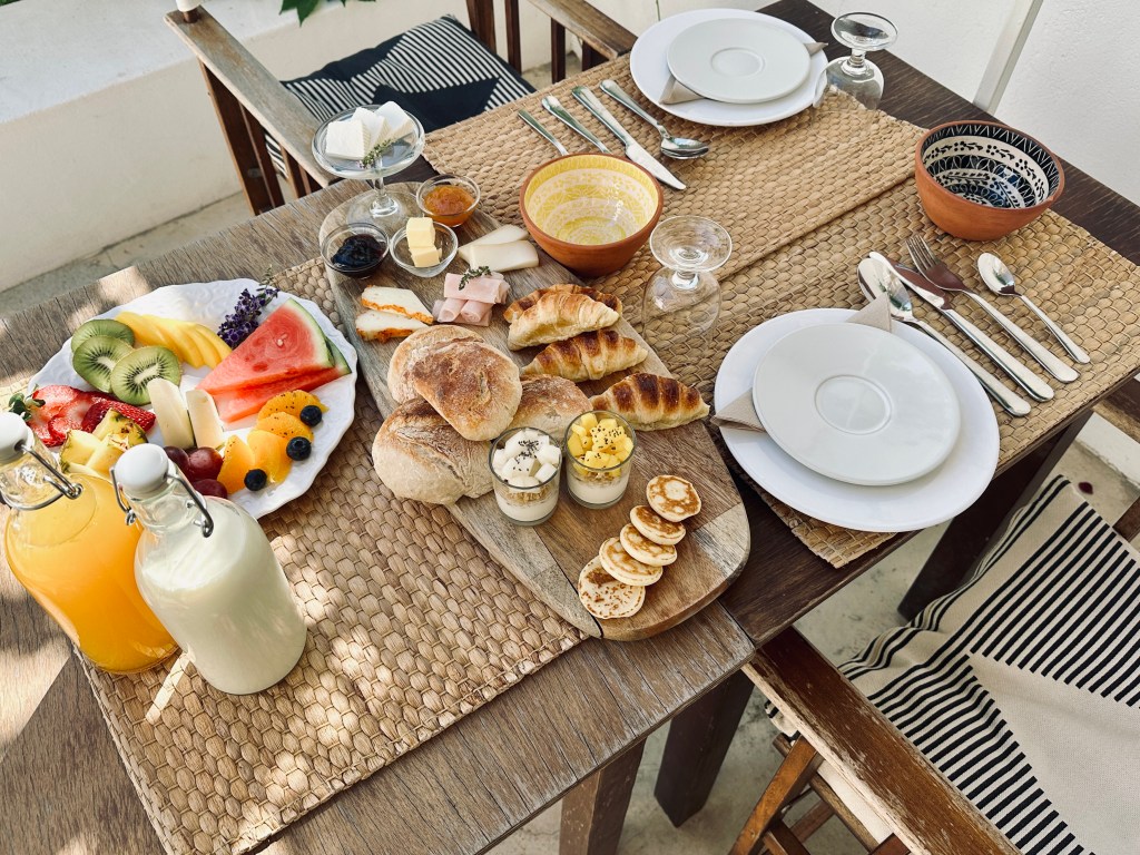 Mesa de café da manhã vista do alto, com frutas, pães, leite e suco de laranja
