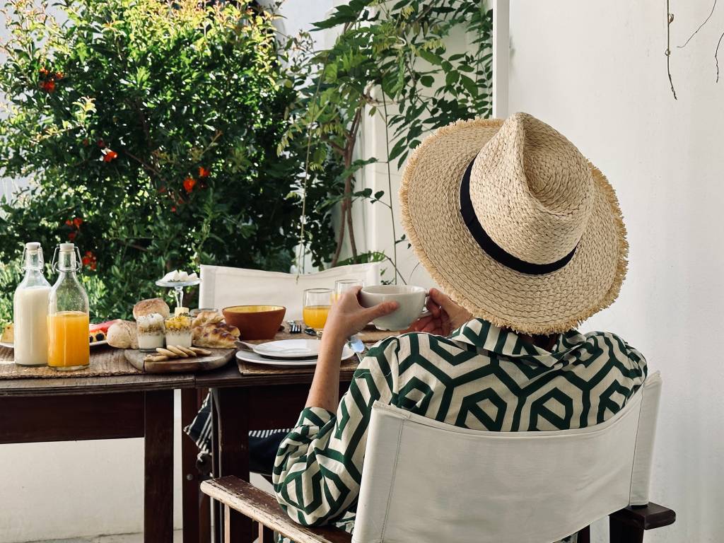 Mulher de chapéu, de gostas, tomando o café da manhã no jardim