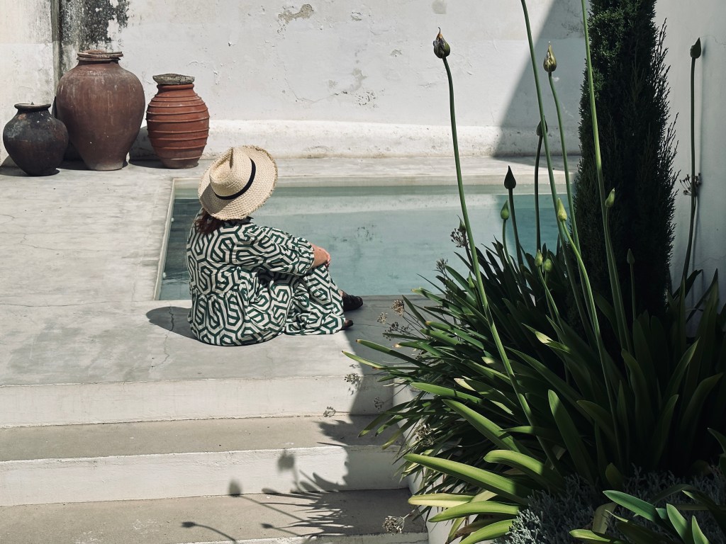 Mulher de chapéu sentada à beira de uma pequena piscina