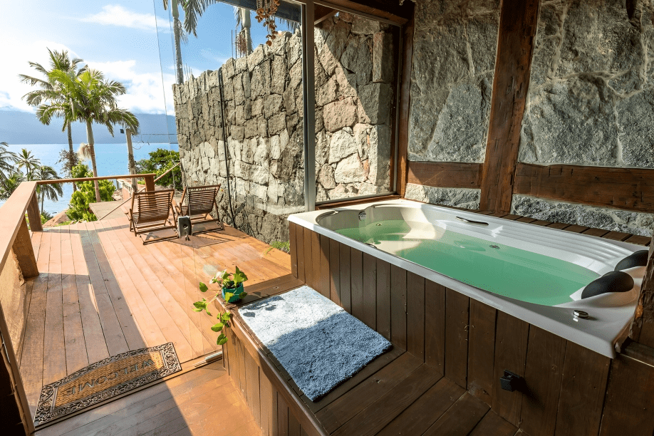 Loft para dois com jacuzzi, Ilhabela, São Paulo, Brasil A foto mostra um deck com uma banheira de hidromassagem e duas cadeiras. A vista é para o mar