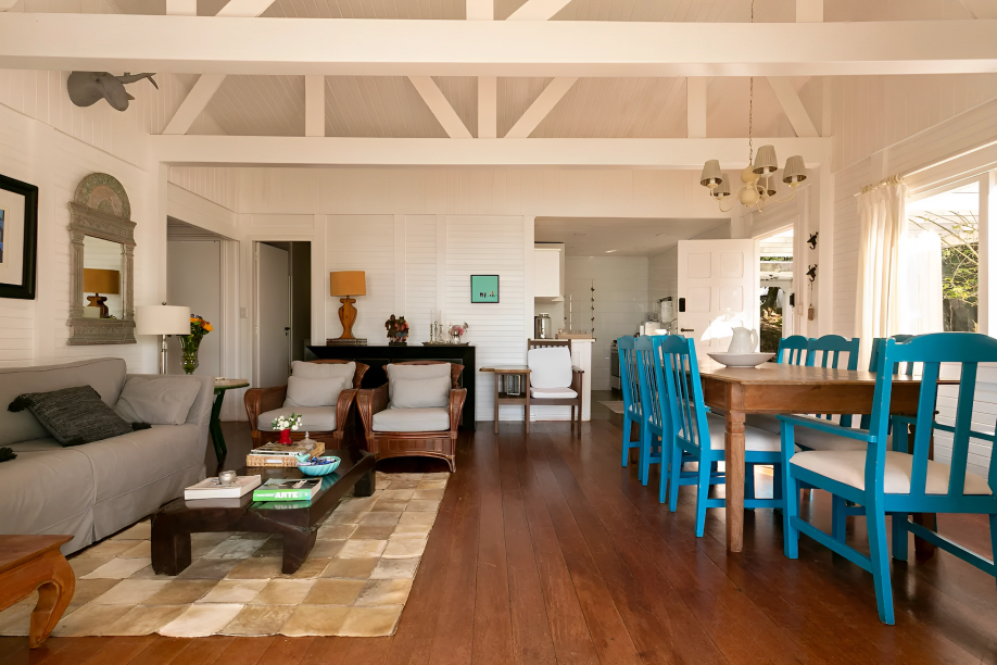 A foto mostra uma sala com piso de madeira e parede de madeira pintada de branco. O espaço é uma sala de estar integrado com área de jantar.