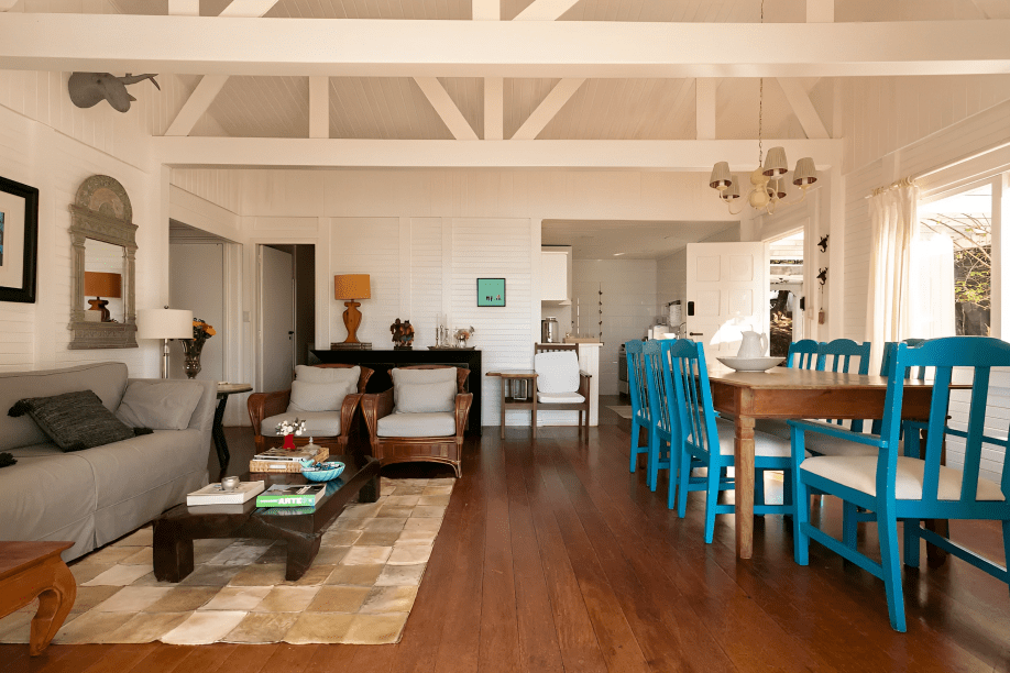 A foto mostra uma sala com piso de madeira e parede de madeira pintada de branco. O espaço é uma sala de estar integrado com área de jantar.