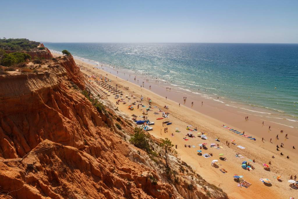 amazing-beach-in-algarve-portugal-albufeira-fal-2023-11-27-05-16-54-utc Foto colorida mostra uma praia vista do alto de suas falésias coloridas. Lá embaixo, banhistas e guarda-sóis se espalham na areia
