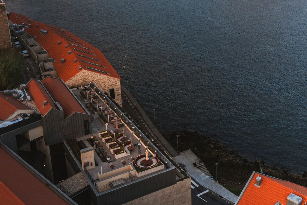 Fotografia aérea mostra o hotel The Rebello debruçado sobre as águas do Douro, destacando o seu rooftop