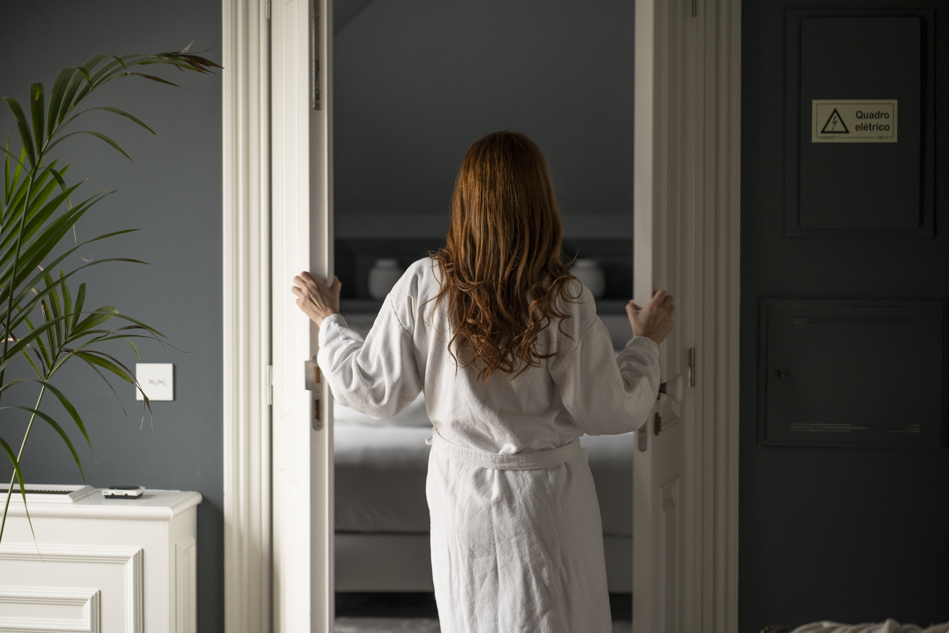 Mulher de roupãp abre uma porta de madeira branca num dos quartos do hotel