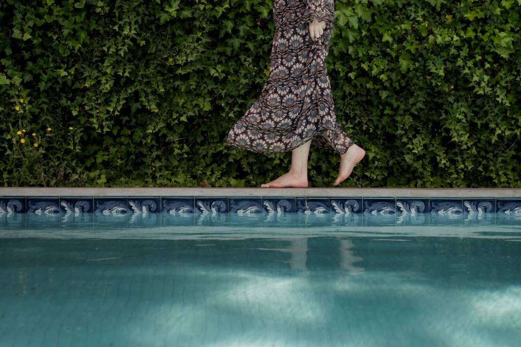 A imagem mostra detalhe da piscina do hotel com os pés de uma mulher caminhando na beirada