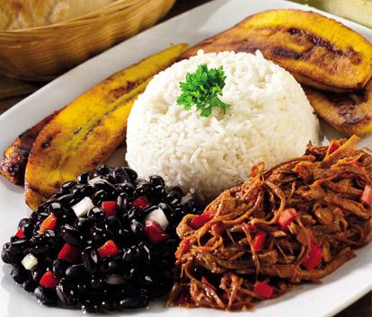 Pabellon_criollo_Venezuela Um prato contendo banana frita, feijão preto, arroz branco e carne desfiada.