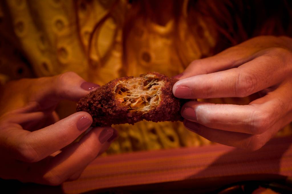 _1NC8750 Imagem fechada nas mãos de uma mulher, que abre um croquete para comê-lo