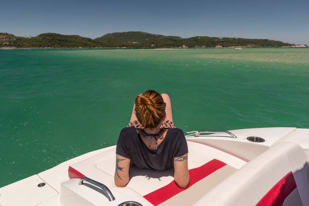 2017_Nuvem-362 Mulher deitada num barco cercado de aguas verde-esmeralda. Ao fundo vê-se montanhas e praias
